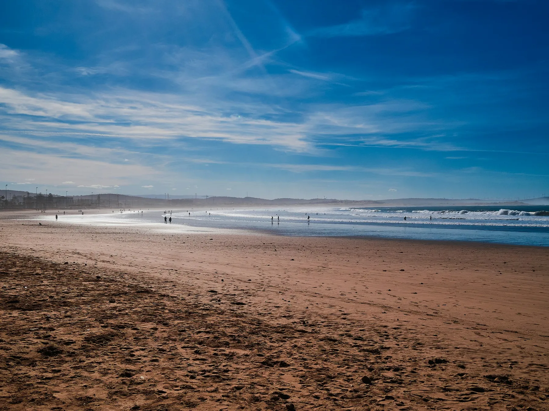 People walking along a Moroccan beach as waves come in.